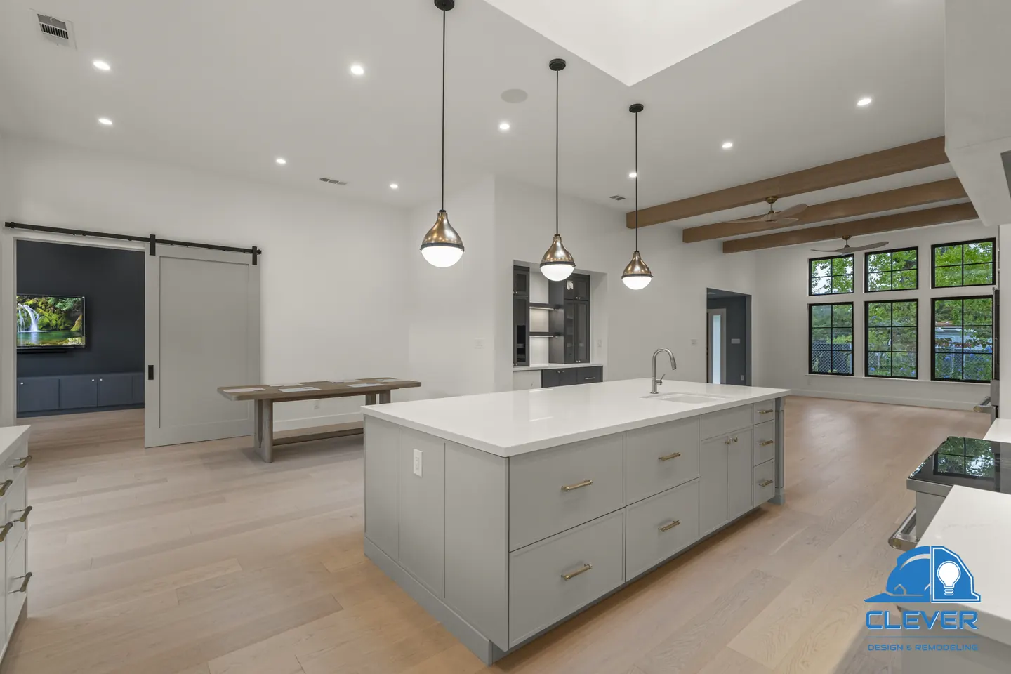 Kitchen island with white quartz and gray cabinets under three brass pendants, with oak beams and a barn door beyond, whole-home remodel in Saratoga, CA